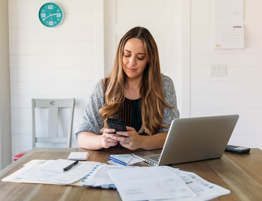 Woman sitting at table managing finances with laptop and mobile device