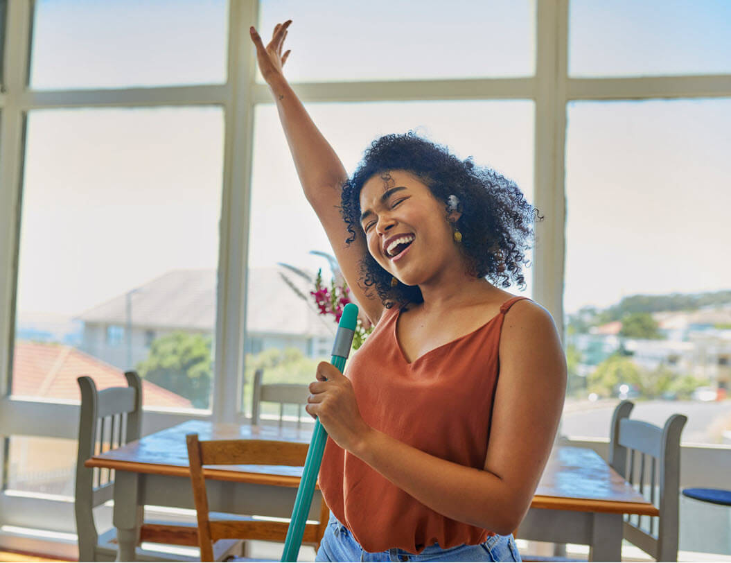 Woman wearing headphones singing while cleaning