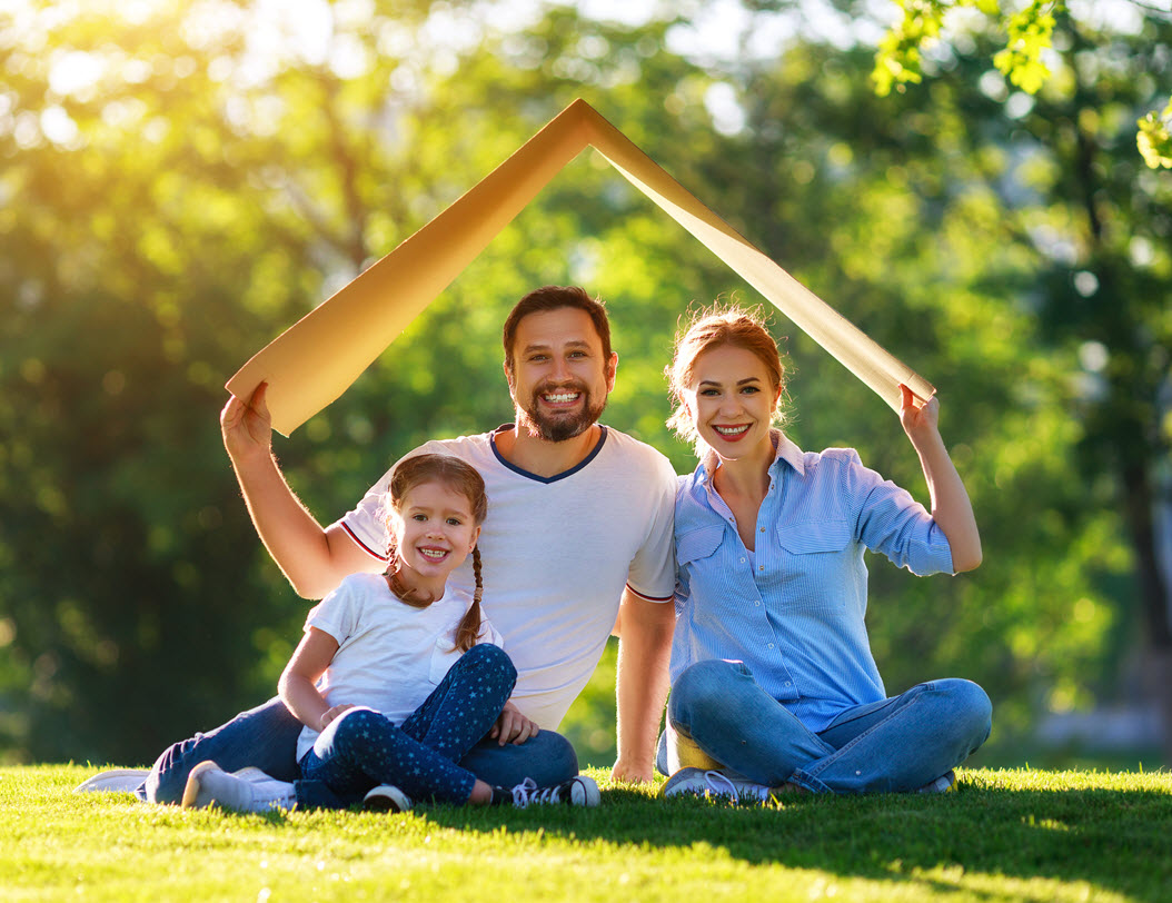 Family sitting under cardboard that looks like a house roof